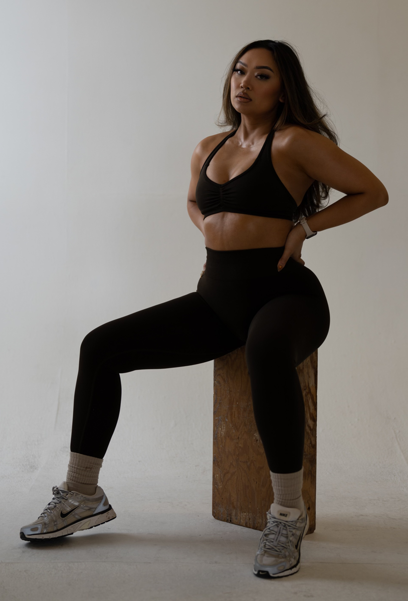 Coach is posing inside a concrete building, in workout outfit, with a hand bag and beverage.